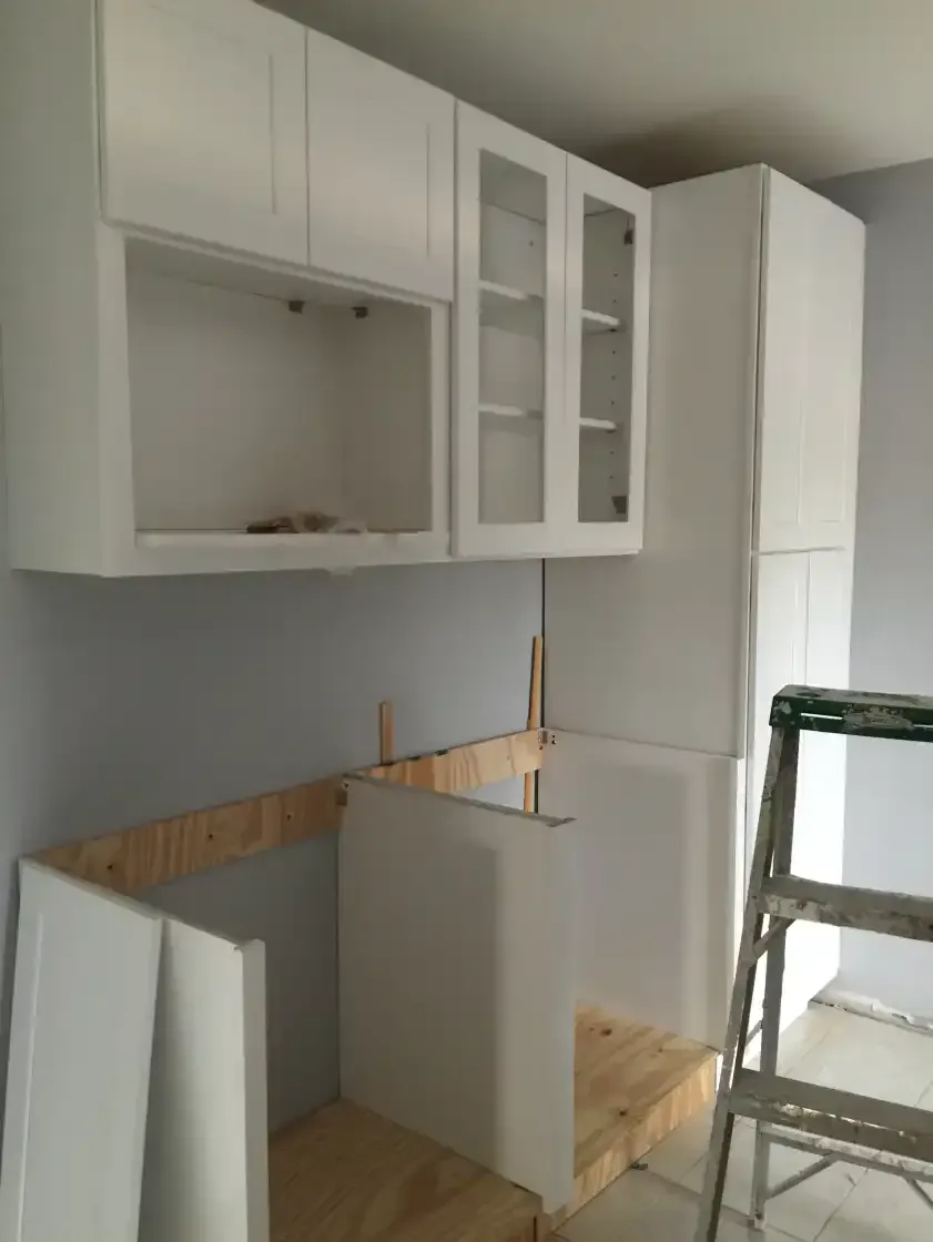 A kitchen under construction with white cabinets and a ladder