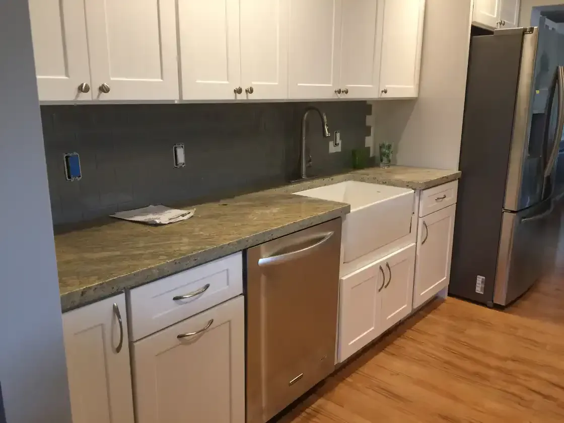 A kitchen with white cabinets , stainless steel appliances , a sink and a refrigerator.