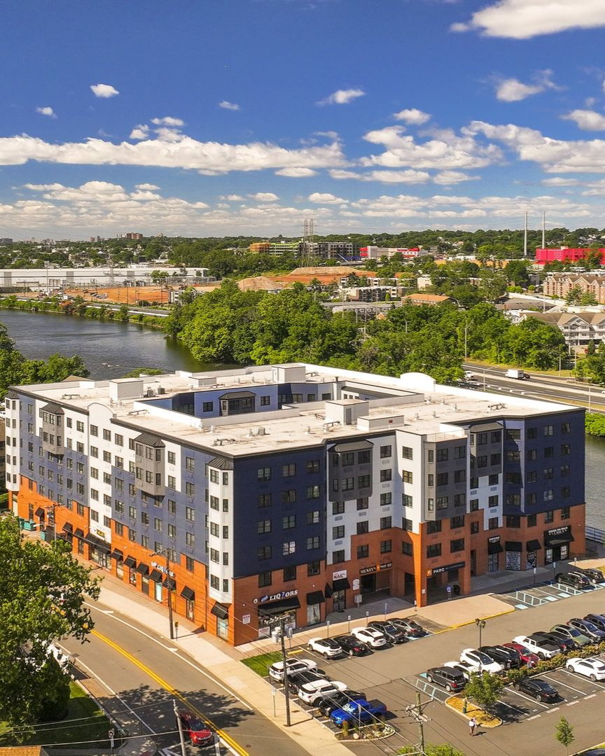 Building with blue awning, pool, and orange umbrellas in front; townhouses in the background.