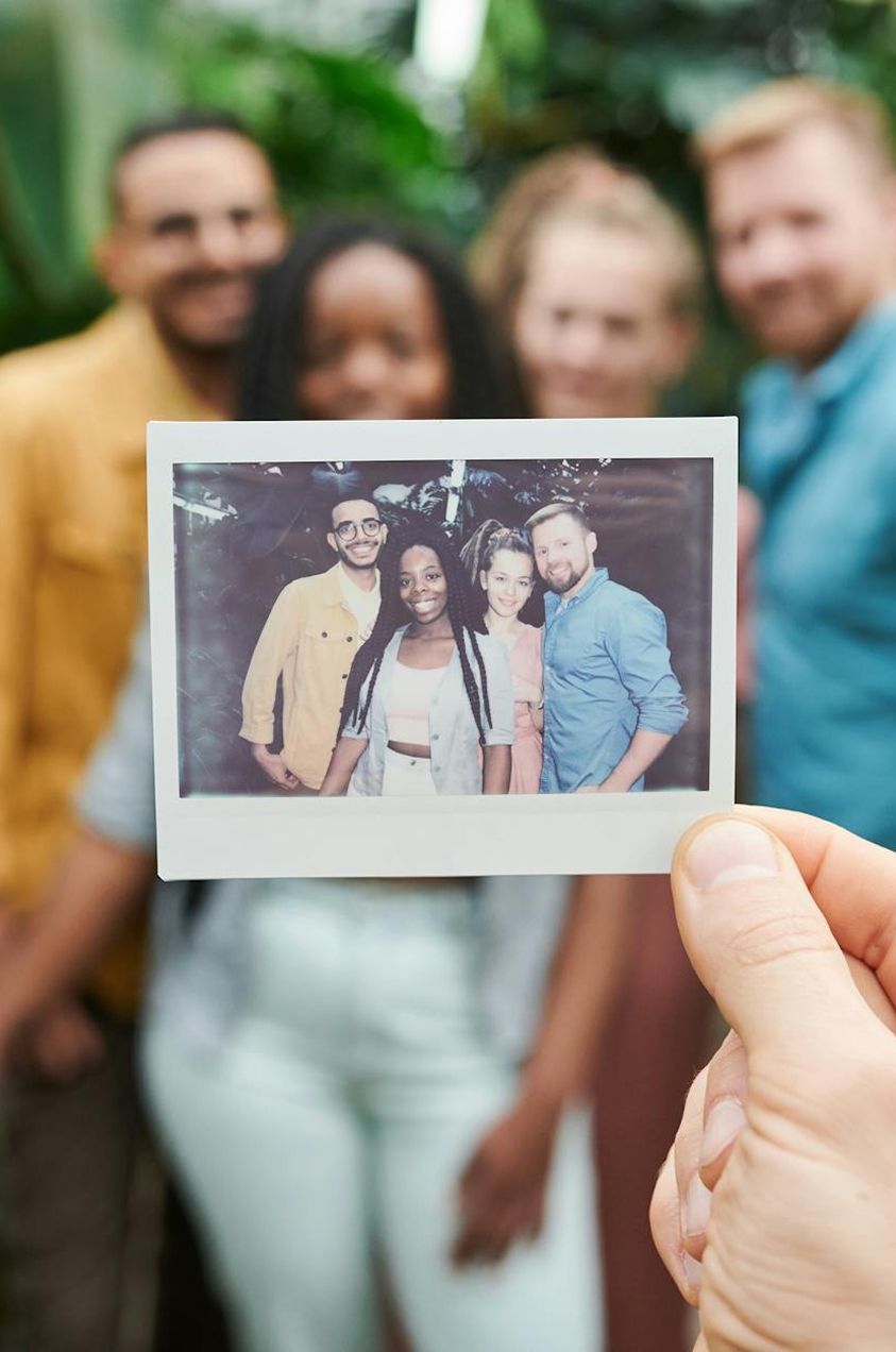 Person holding Polaroid photo of smiling friends outdoors.