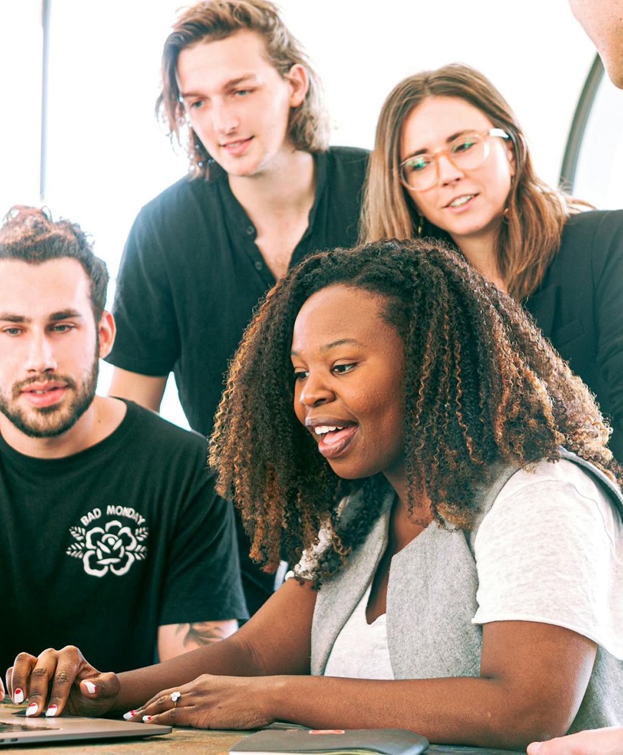 Group of people around a laptop, looking and pointing. The person working is smiling.