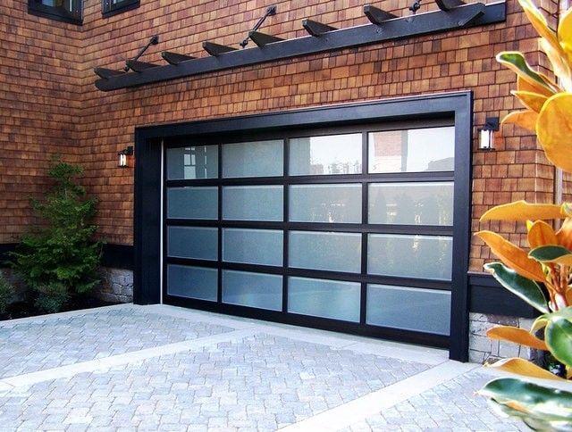 Garage with a glass door, framed in silver, between two stone pillars. The driveway is paved.