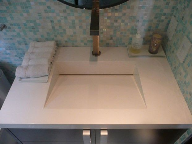 Modern bathroom vanity with white integrated sink, stacked white towels, copper faucet, and mosaic tile backsplash.