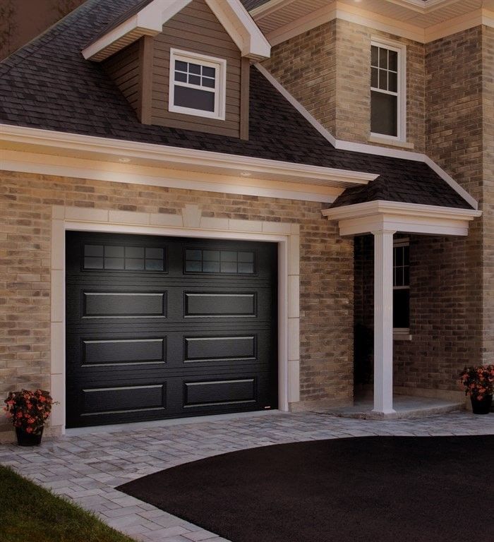 Black garage door on a brick house, with a dark asphalt driveway and small flower pots.