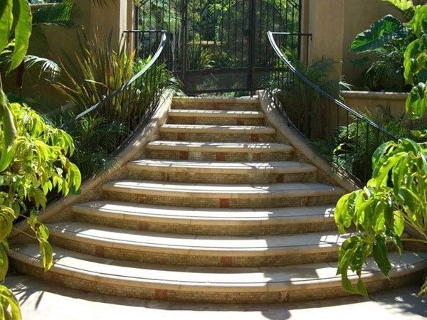 Curved stone steps leading up to a wrought iron gate, with lush greenery on either side.