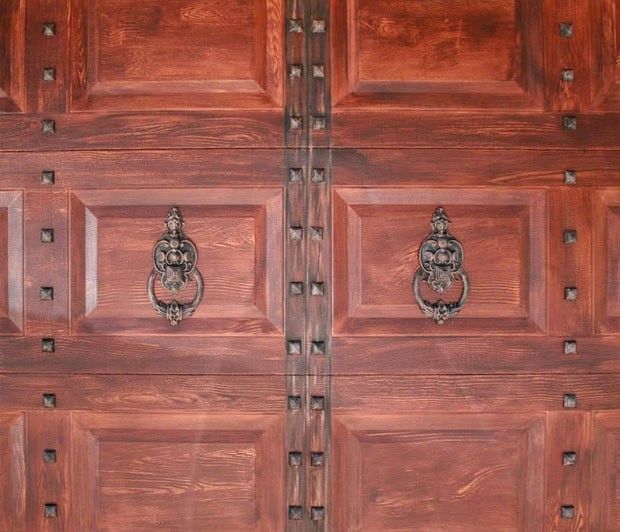 Close-up of a heavy, ornate wooden door with two decorative knockers and metal studding.