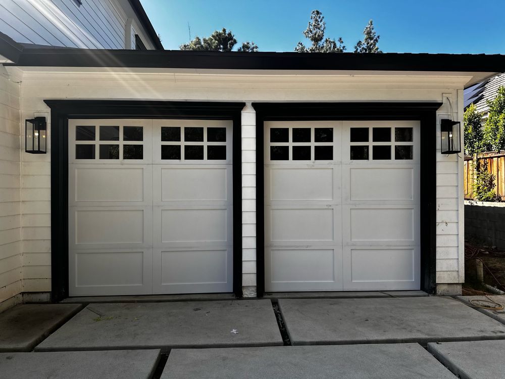 Two white garage doors with black trim and matching black outdoor sconces.