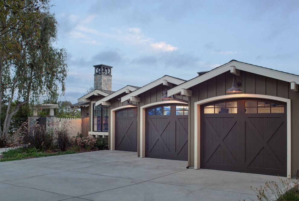 Three-car garage with dark brown doors and a stone chimney in front of a cloudy sky.