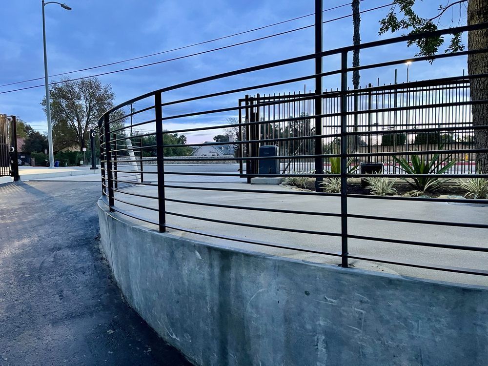 A curved concrete platform with black railings, next to an asphalt road. A dark sky is overhead.