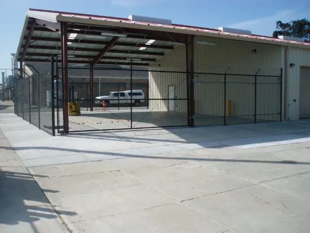 Warehouse with a security fence and covered loading area; a white van is visible inside.