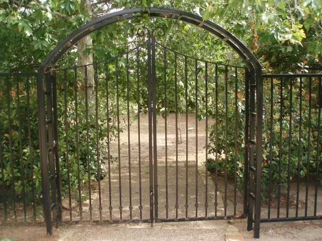 Black wrought iron gate and archway leading into a garden.