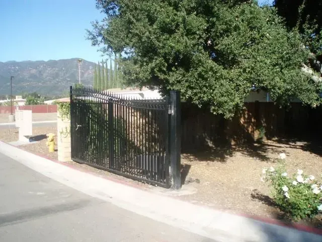 Black metal gate, possibly for a property, with trees and a mountain in the background.