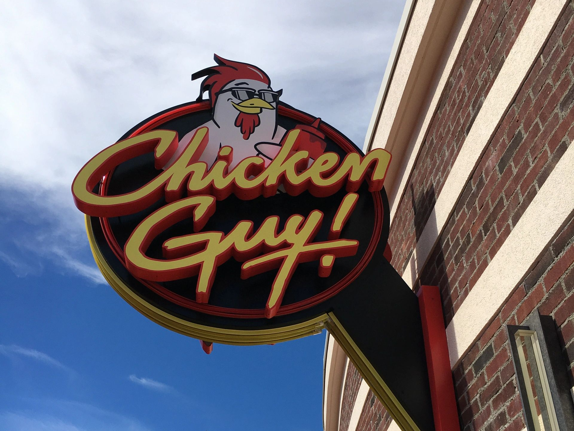 A chicken guy sign hangs from the side of a brick building