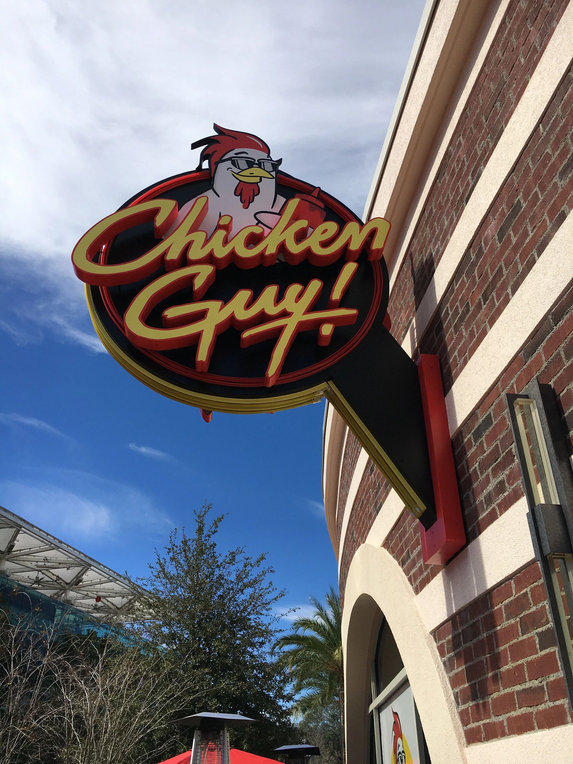 A chicken guy sign hangs on the side of a brick building