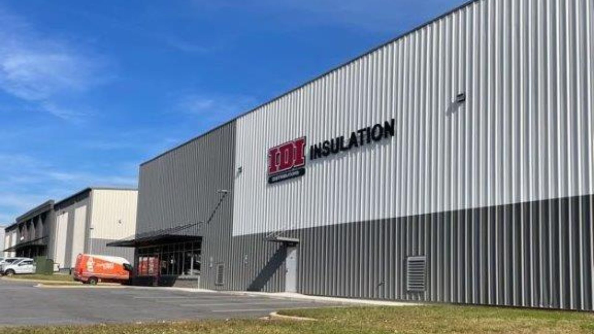 A modern industrial warehouse building with grey and white metal siding, featuring the Fox Insulation logo on the front.