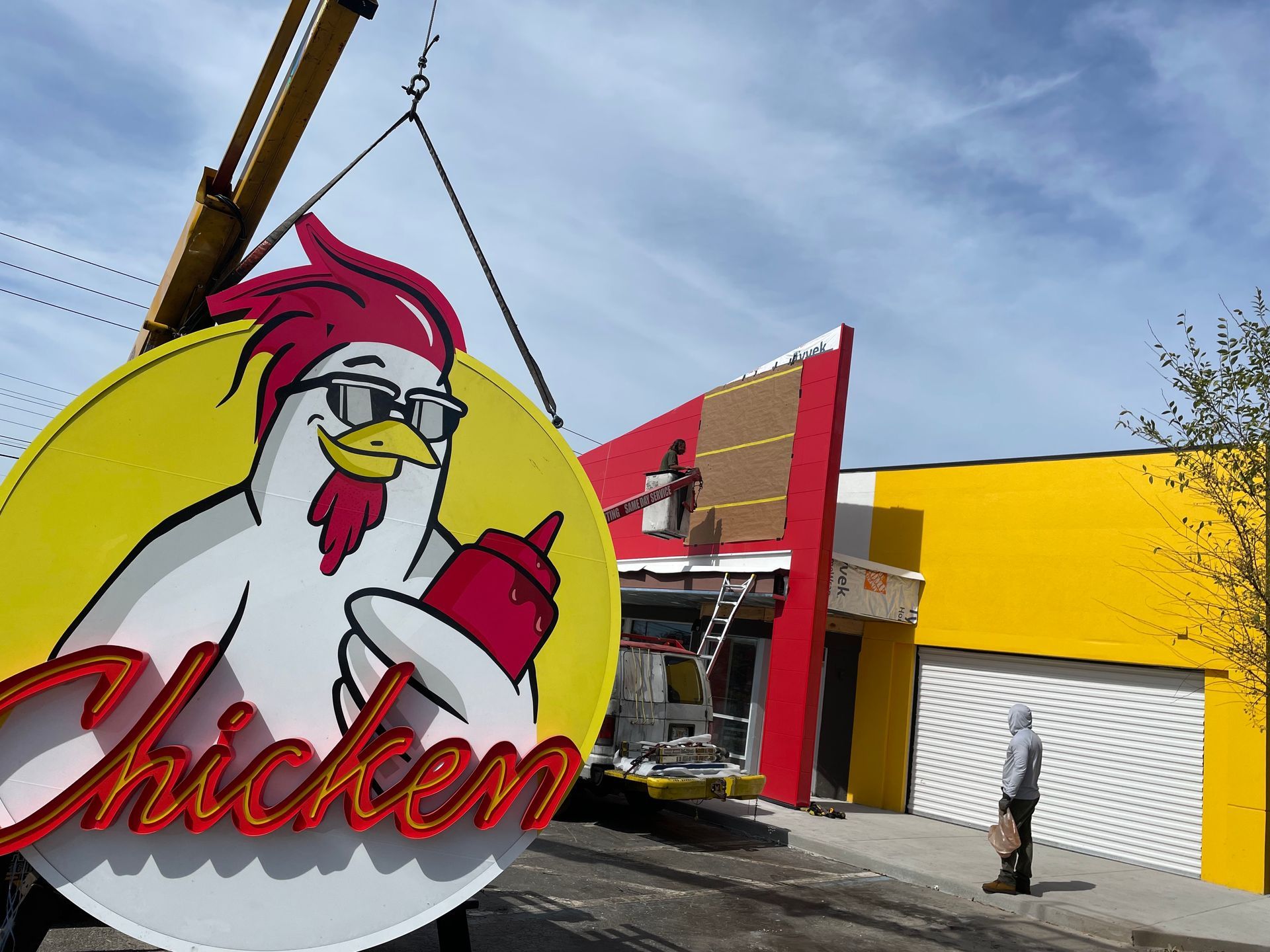 A large chicken sign is being lifted by a crane