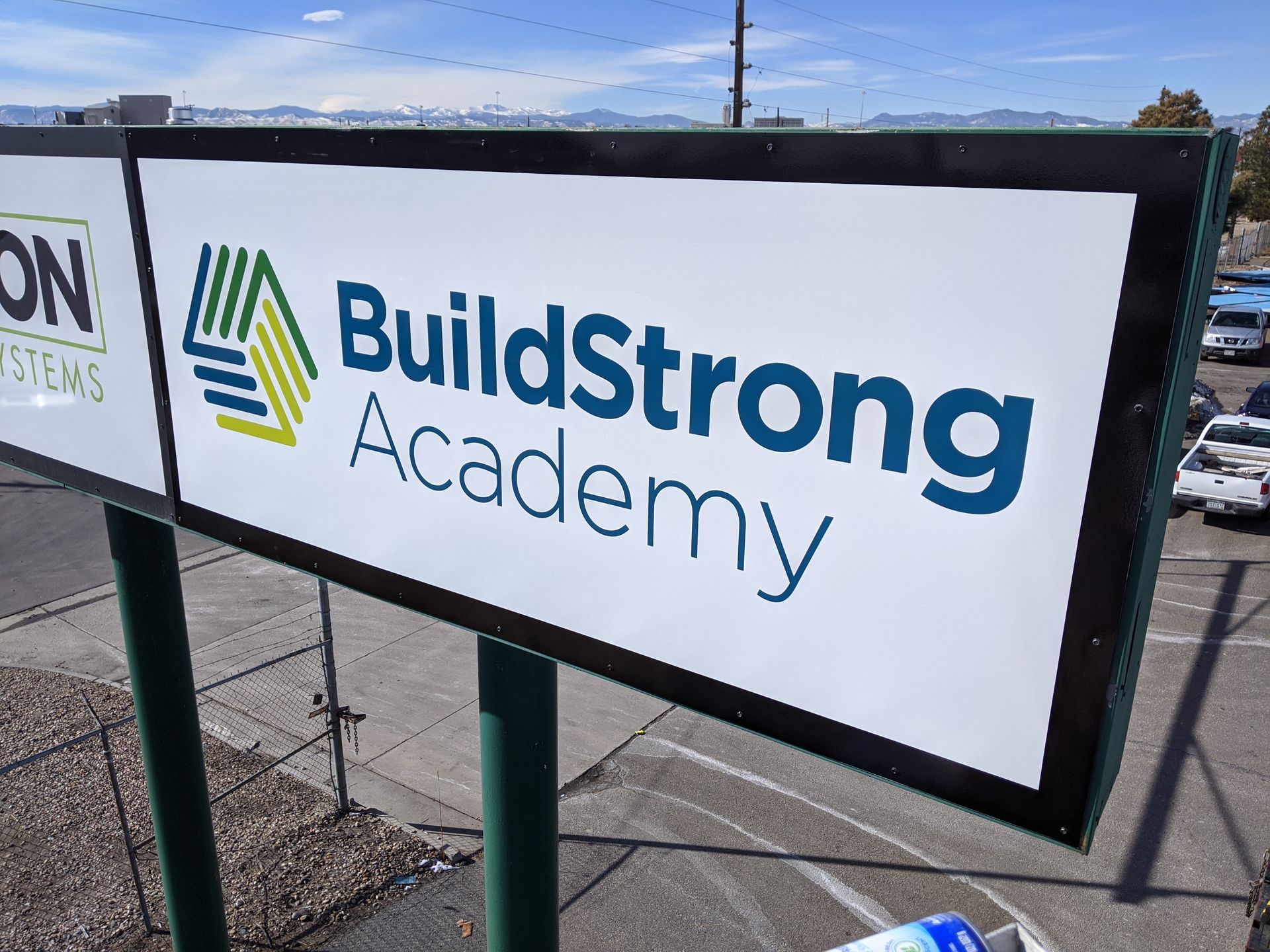 A sign for buildstrong academy is sitting on top of a green pole.