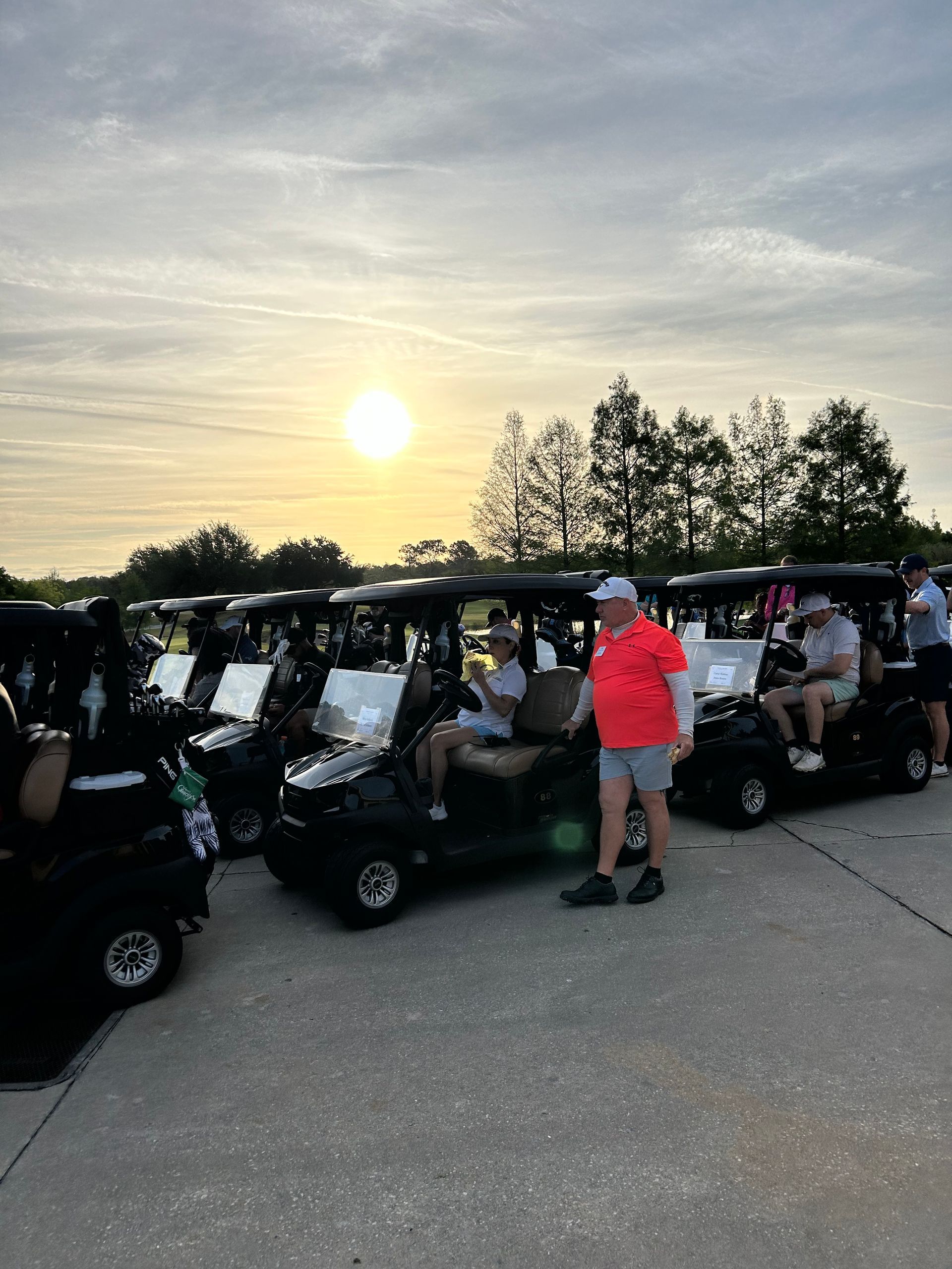 A man in a red shirt is standing in front of a row of golf carts.