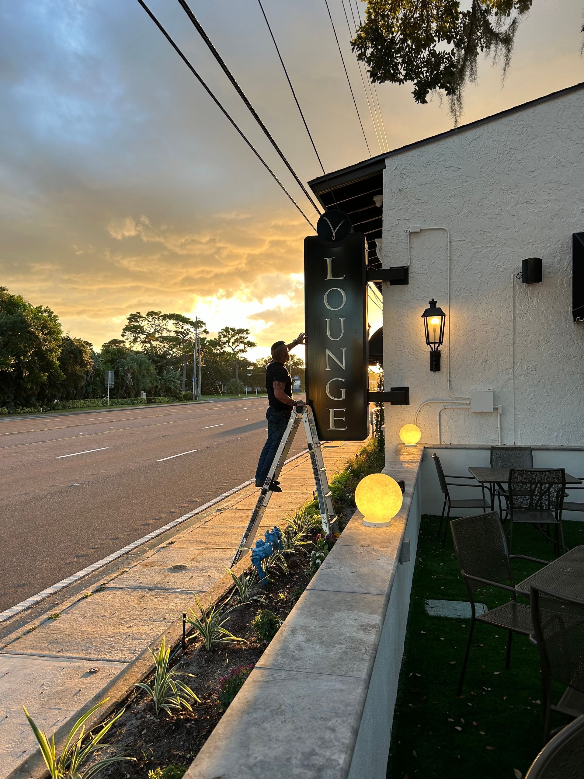 A man is standing on a ladder next to a sign that says ' enzo ' on it.
