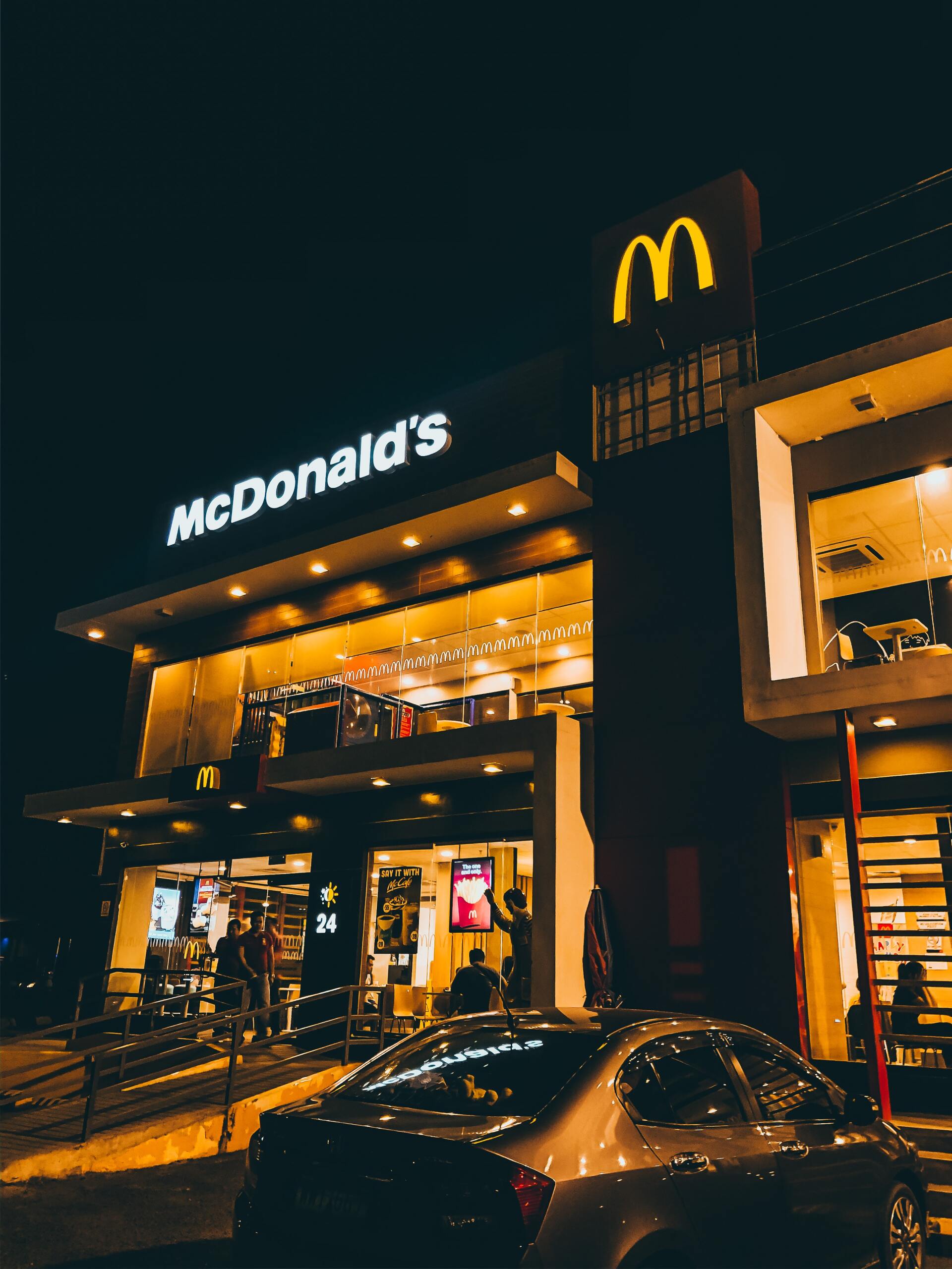 A car is parked in front of a mcdonald 's restaurant at night.