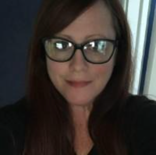 A man in a suit and tie is standing in front of a tree.