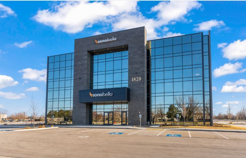 Modern glass office building with dark stone center and blue sky reflected in windows