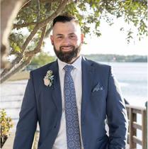 A man in a suit and tie is standing in front of a tree.