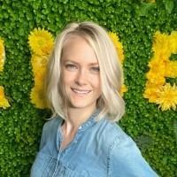 A woman in a blue shirt is standing in front of a green wall with yellow flowers.