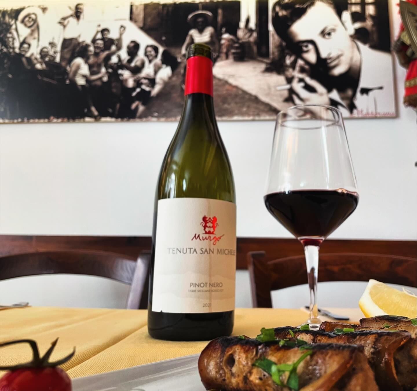 Una bottiglia di vino con un'etichetta bianca e un tappo rosso è su un tavolo accanto a un bicchiere di vino