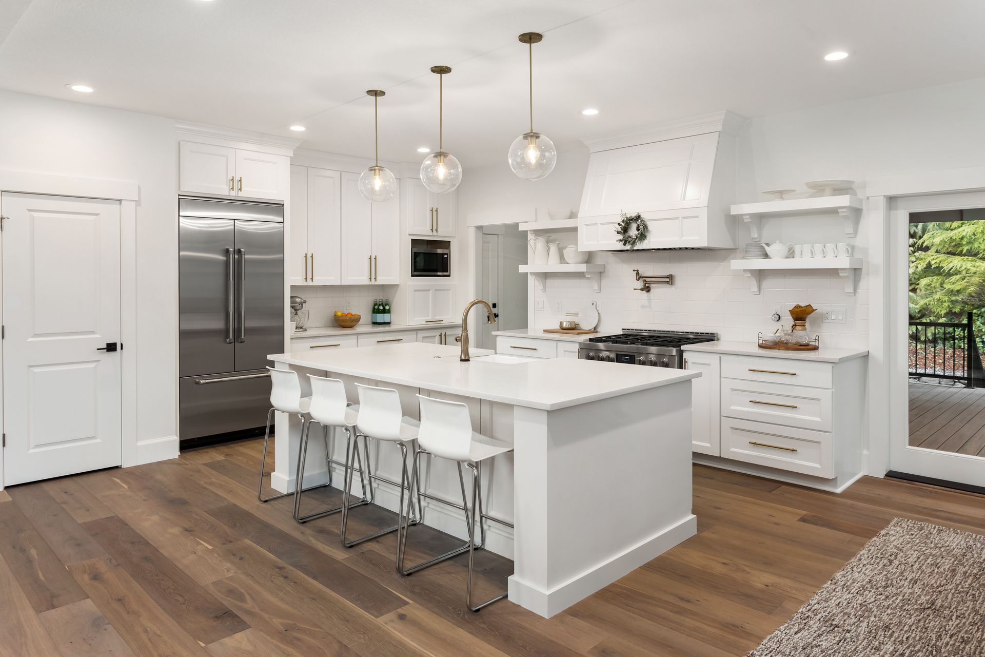 Modern white kitchen with wood floors. Features island with seating, stainless steel appliances, and pendant lights.