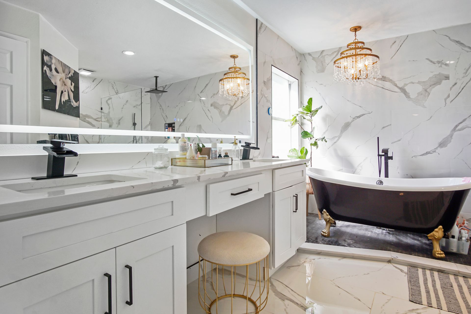 A luxurious white bathroom with marble-look walls, a dark clawfoot tub, and two crystal chandeliers.