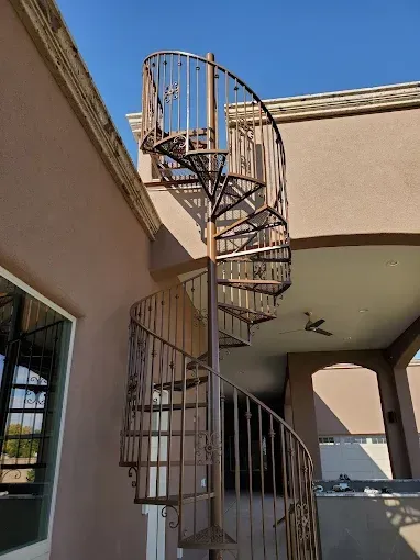 Outdoor spiral staircase with metal railings beside a beige stucco building under an overhang