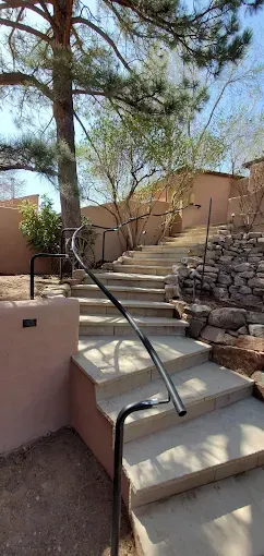 Outdoor stone steps with handrails and adobe walls on a sunny hillside path