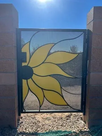Yellow sunflower design on a decorative metal gate between brick pillars in bright sunlight