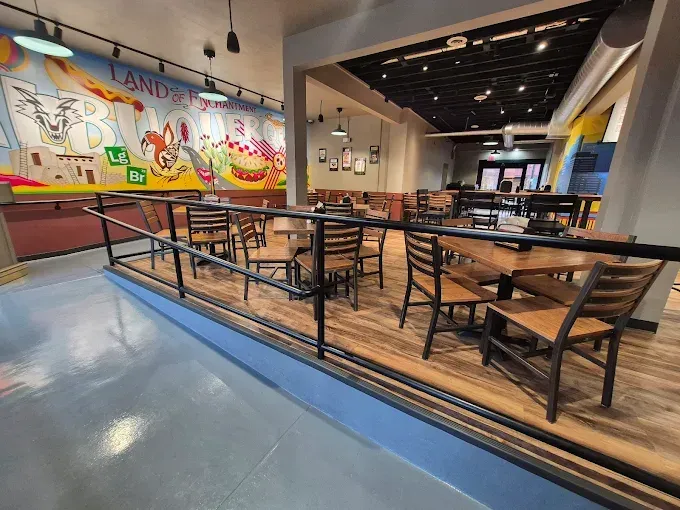 Empty indoor dining area with tables, chairs, and a colorful mural wall.