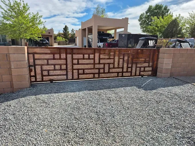 Decorative brick wall with geometric pattern in front of a gravel driveway and carport entrance