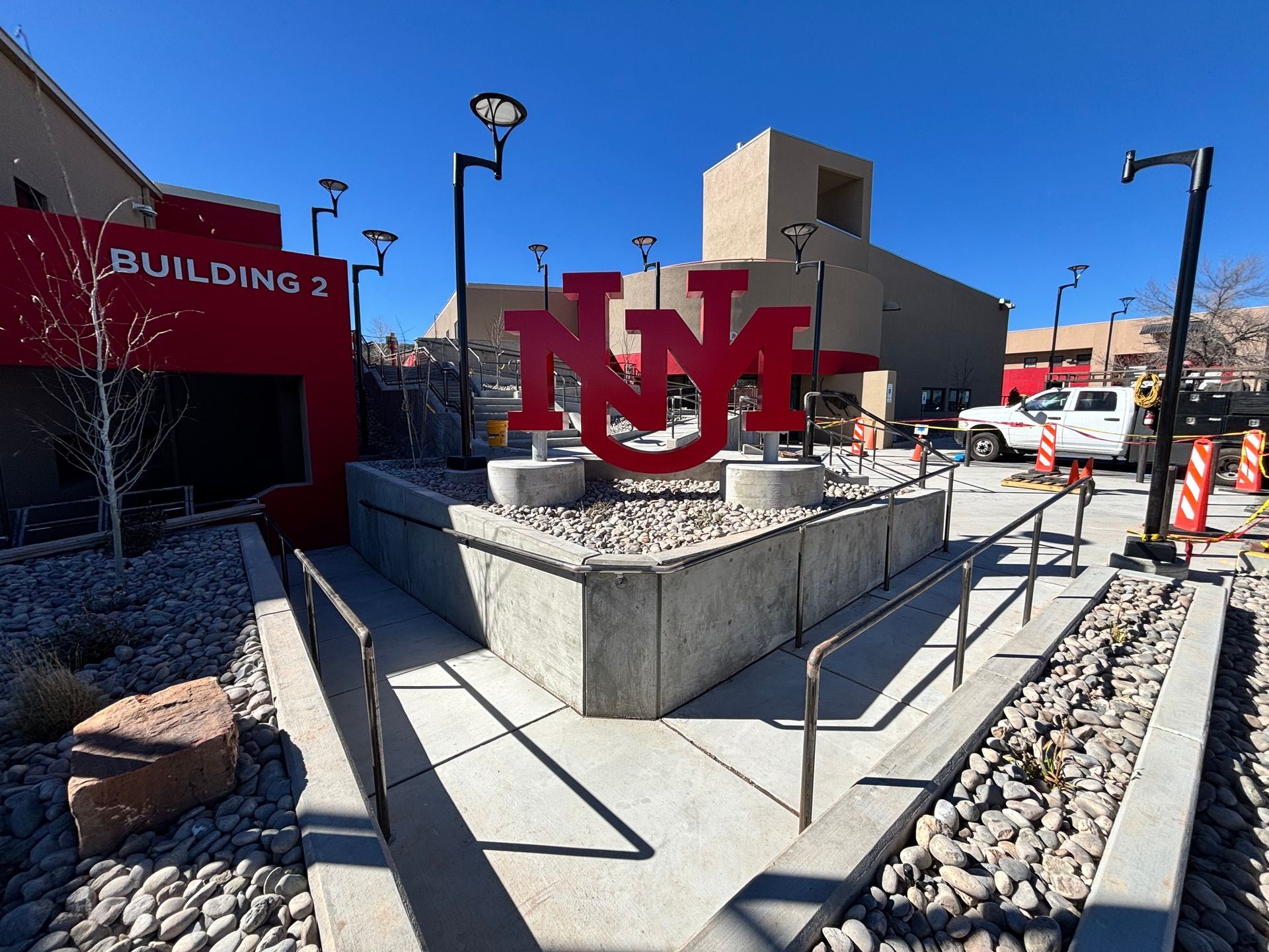 Red UNLV sign outside Building 2 on a sunny campus walkway, with rocks and railings nearby