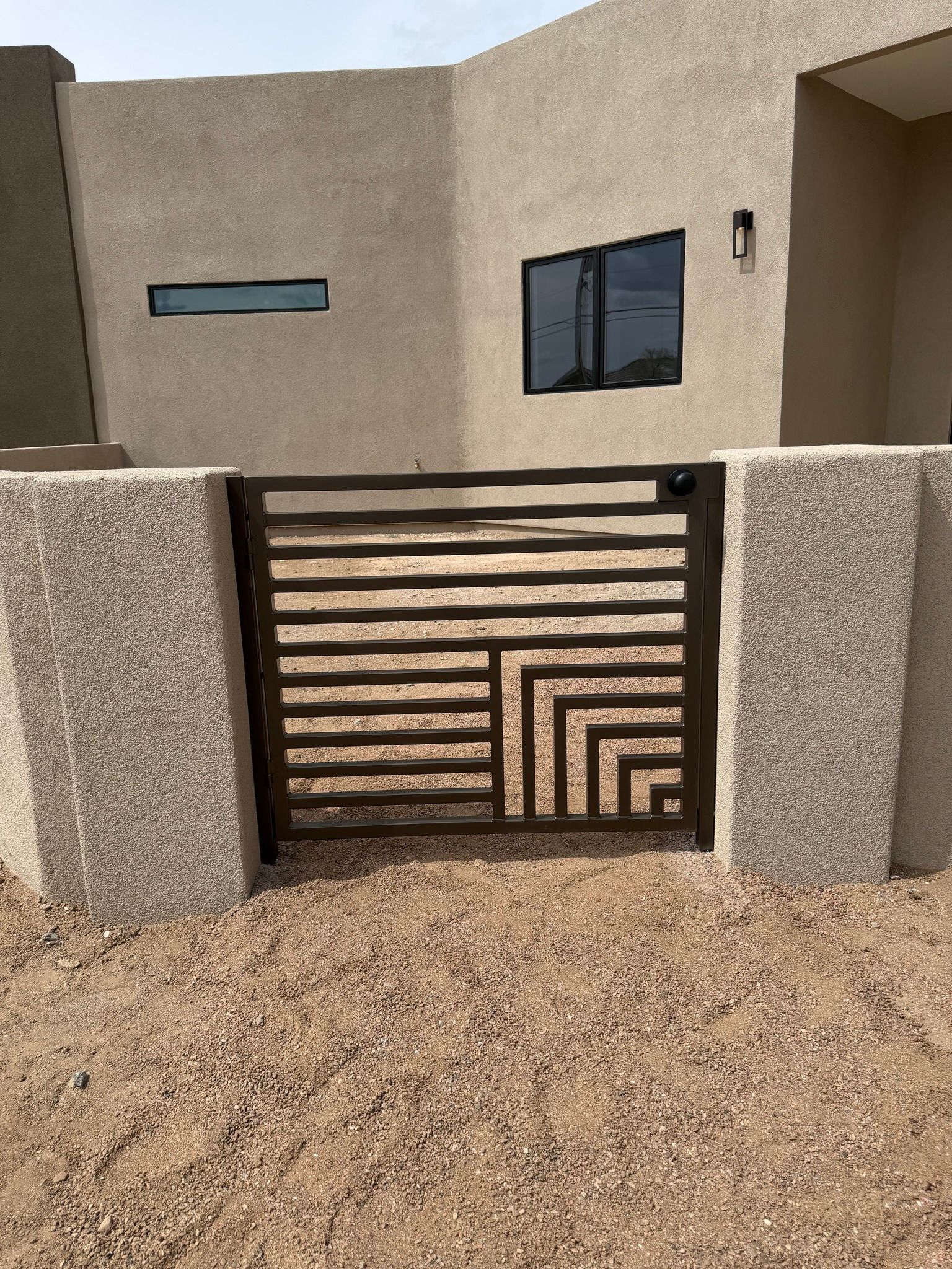 Modern house facade with a striped metal gate, beige walls, and gravel front yard