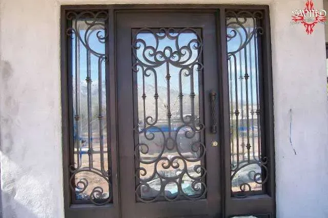 A brown metal front door with decorative iron scrollwork panels and glass, flanked by matching sidelights.