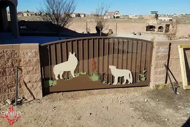 Coyote-themed metal gate art in a desert yard, with two white coyote silhouettes and painted rocks.
