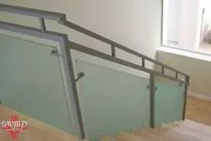 Indoor stairway with frosted glass railings and a metal handrail beside a window.