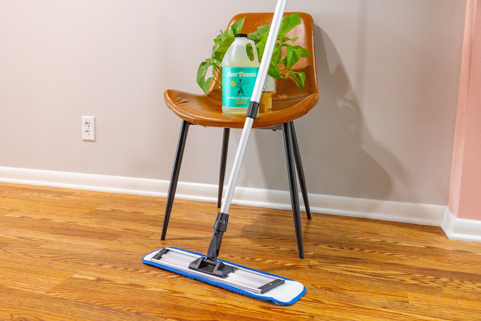 A mop is sitting on a wooden floor next to a chair.