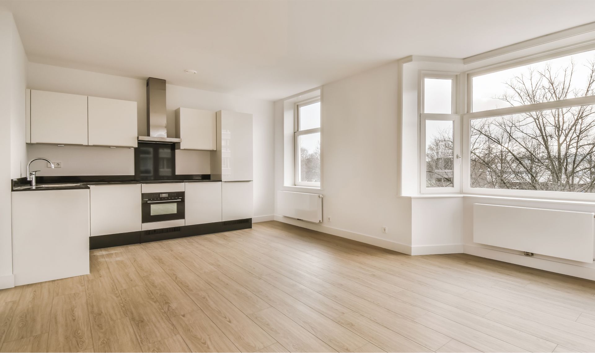 An empty kitchen with a wooden floor and white cabinets.