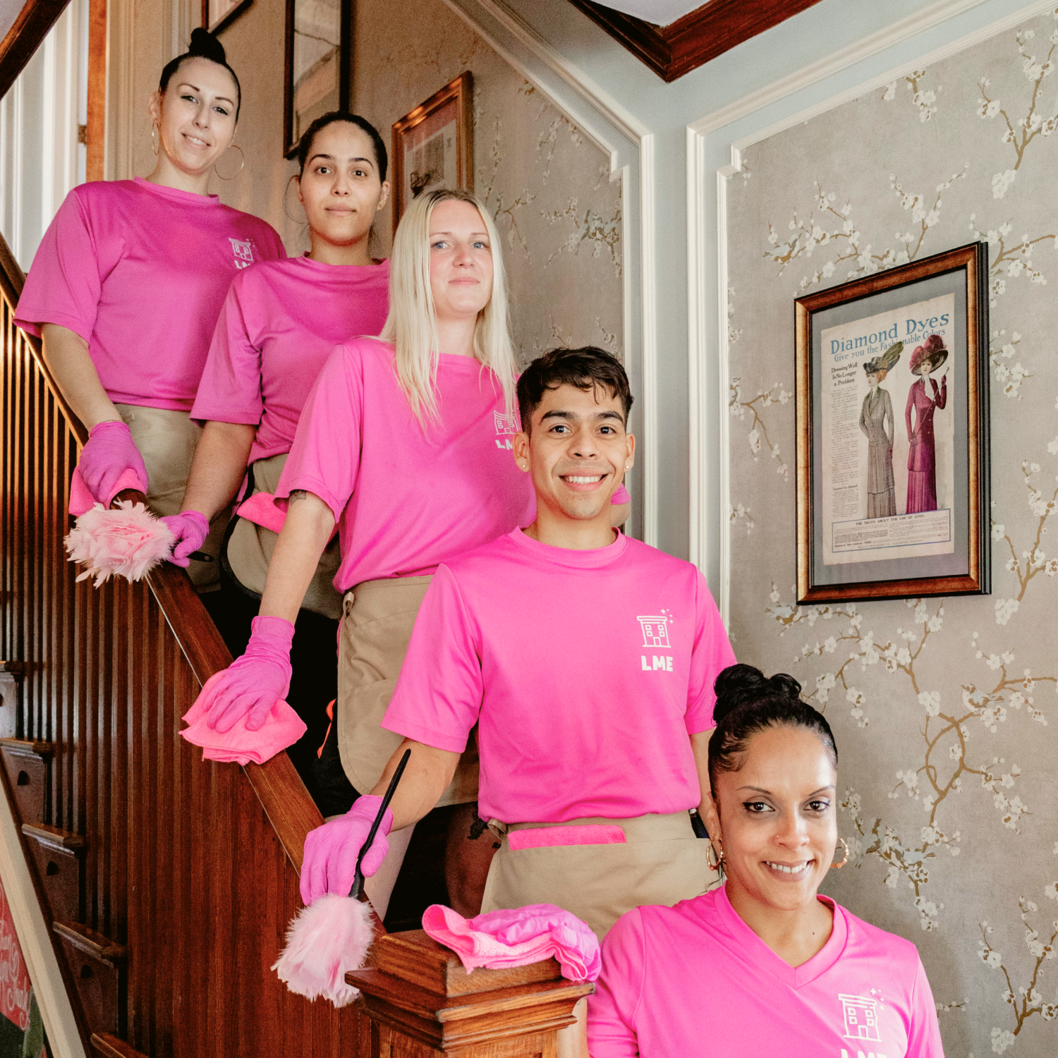 Team of Life Maid Easy cleaning technicians in pink uniforms and gloves on a staircase, showcasing professionalism and teamwork in a home setting, emphasizing the company's commitment to quality cleaning services in Philadelphia, PA and Lehigh Valley, PA.