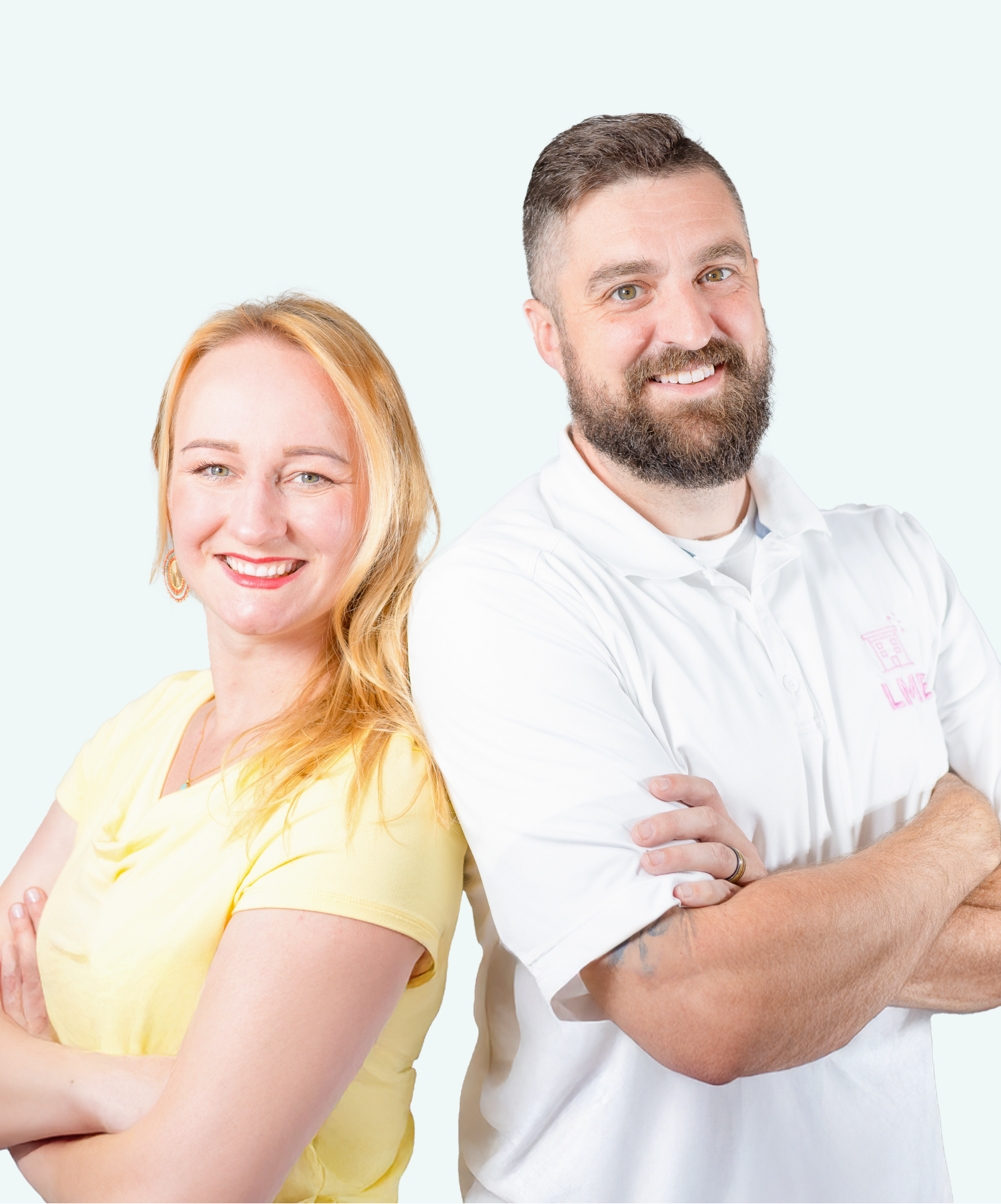 Woman with blonde hair and man with a beard standing back to back, arms crossed, both smiling.