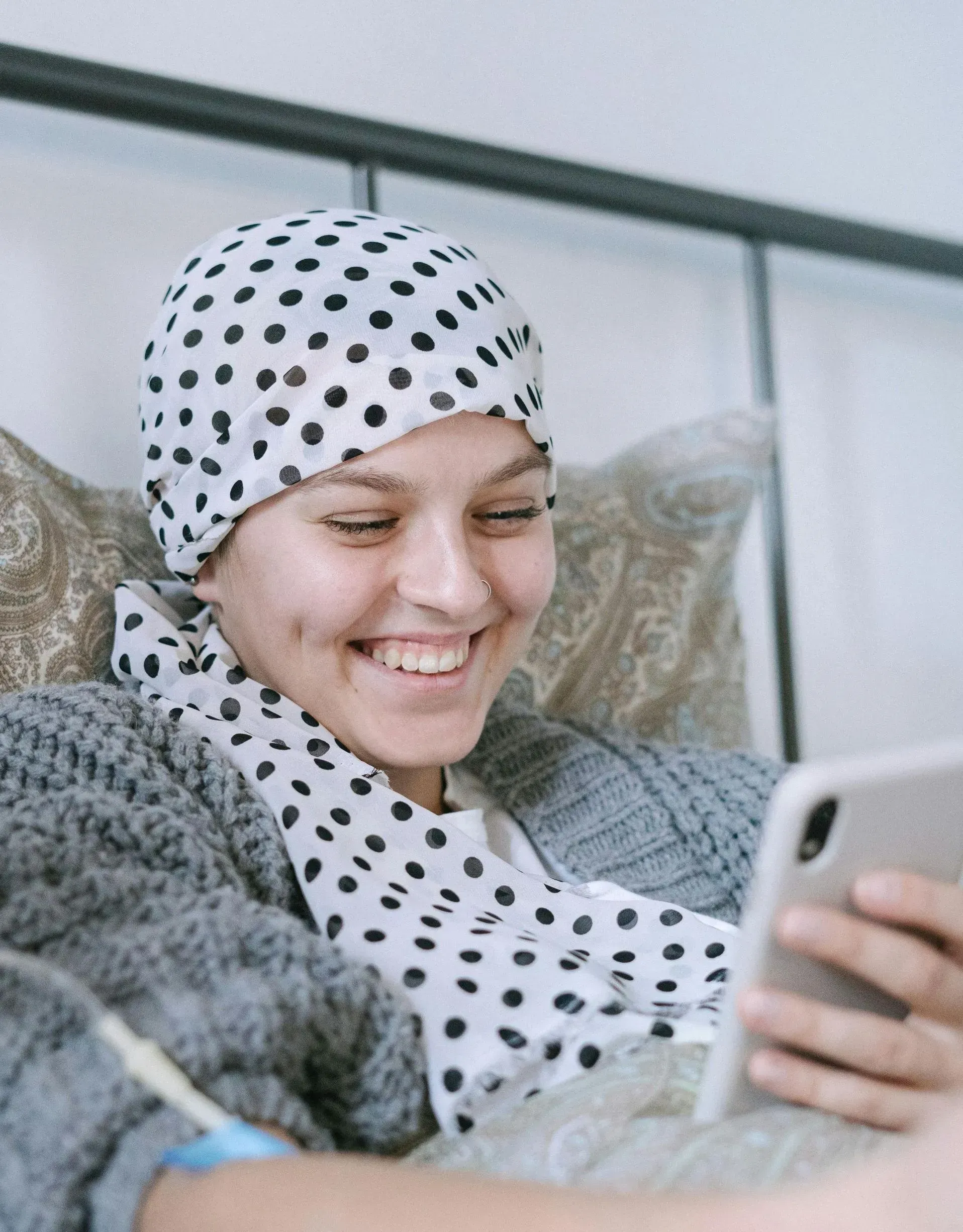 A woman with cancer is laying in bed looking at her cell phone.