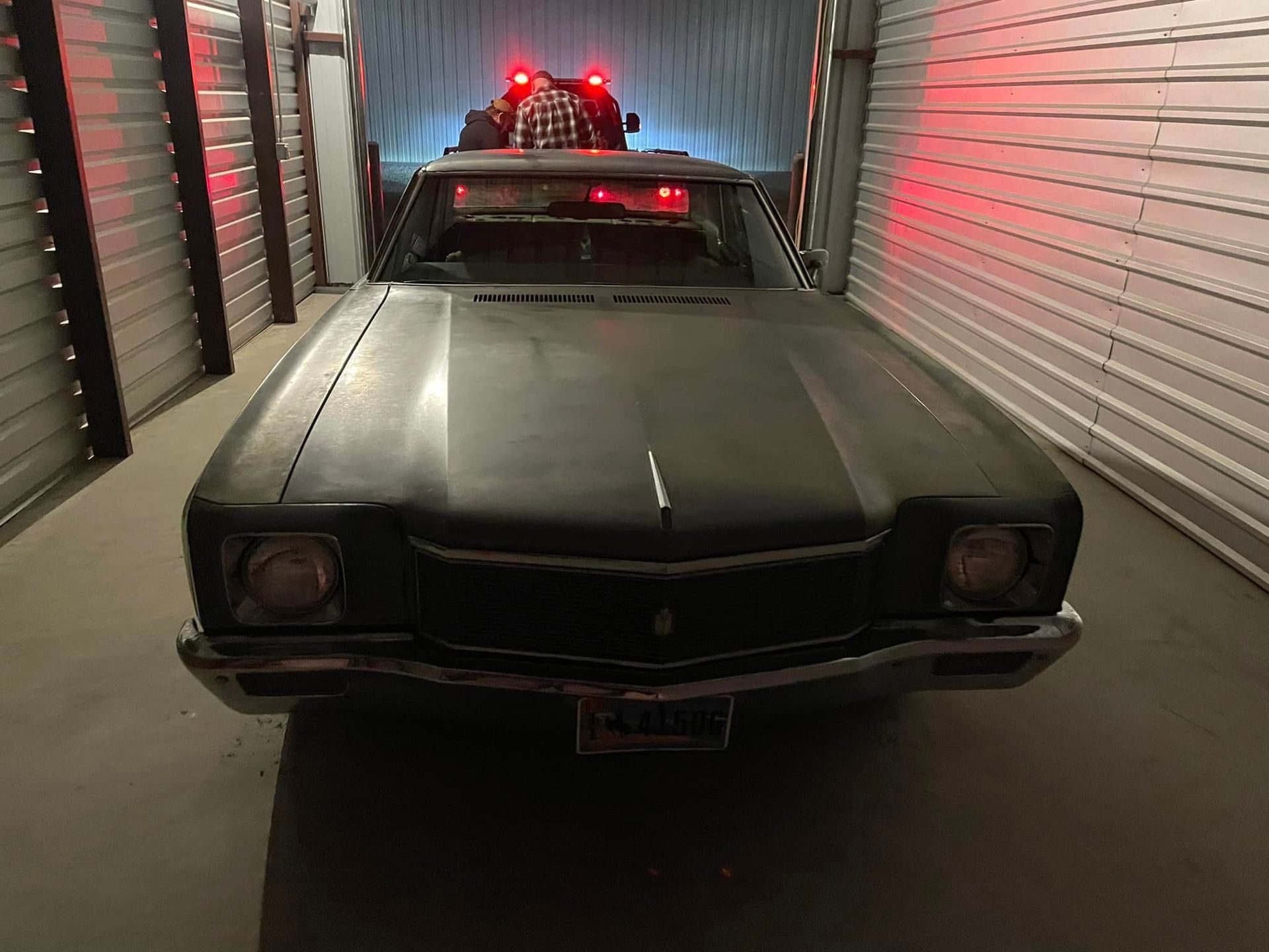 Dark green vintage car with flashing red lights, inside a storage unit.