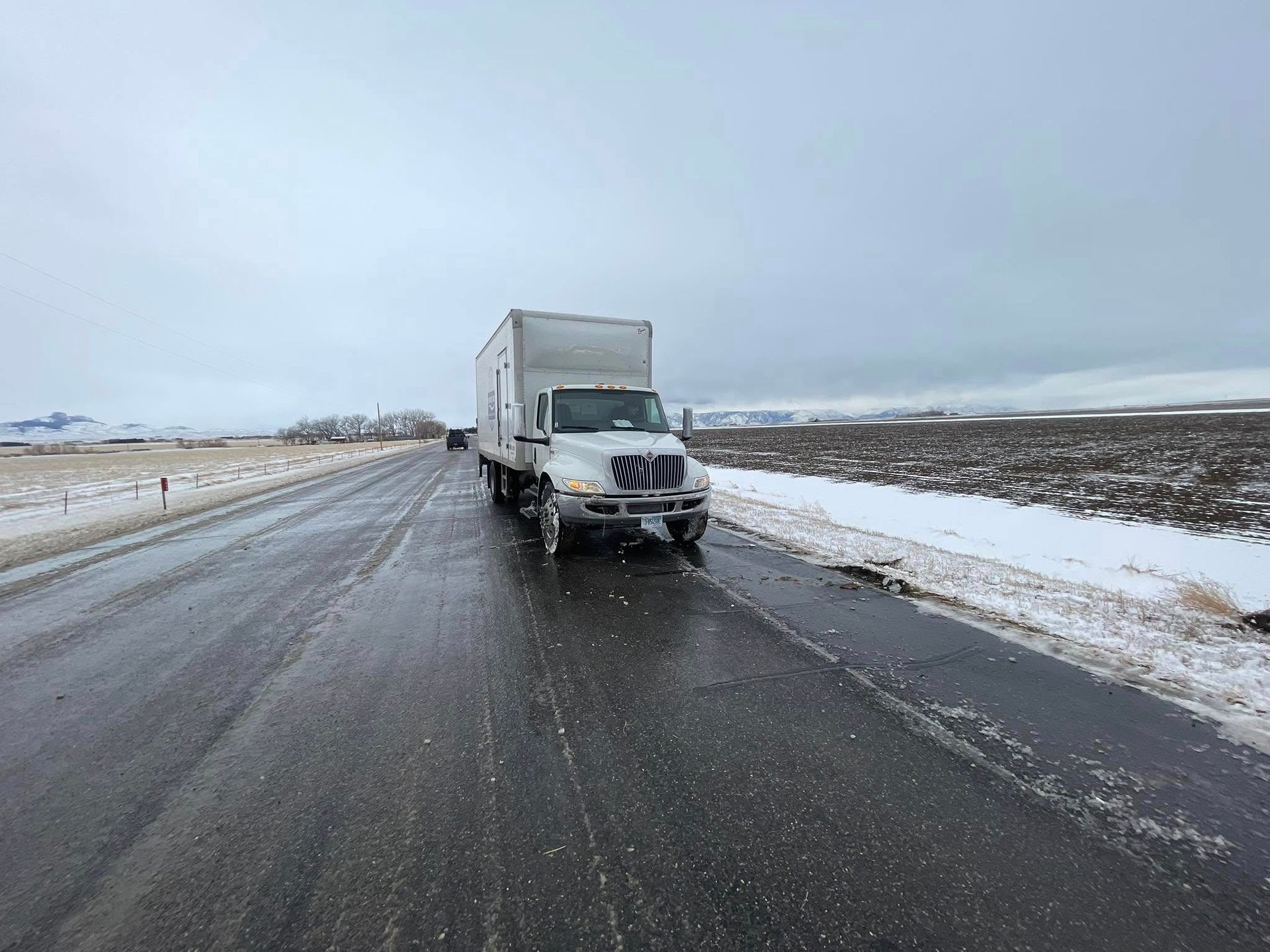 Semi-truck driving on a snow-covered highway. Winter landscape with gray sky and snow-lined shoulder.