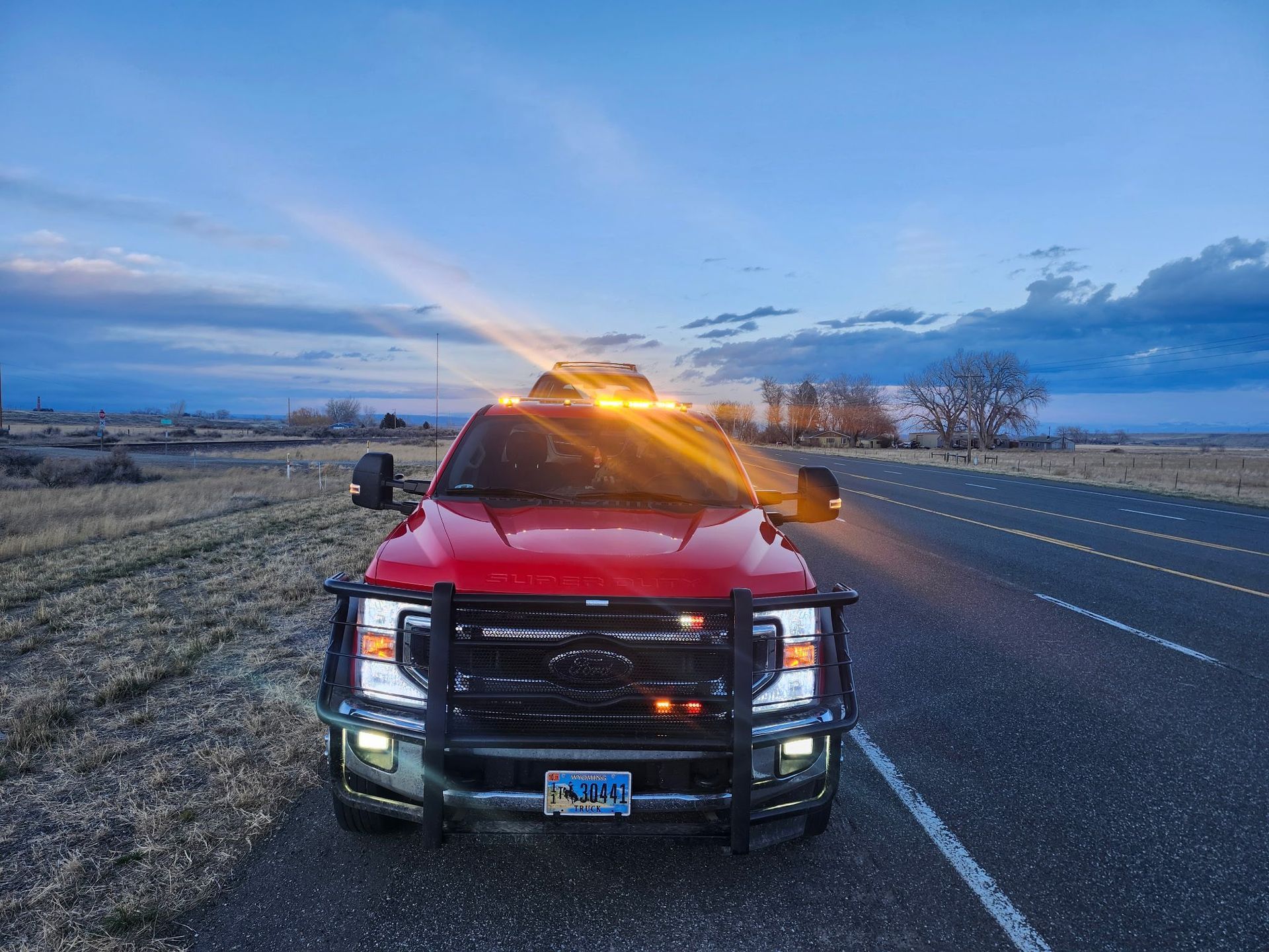 Red pickup truck with emergency lights on, parked on a road at dusk.