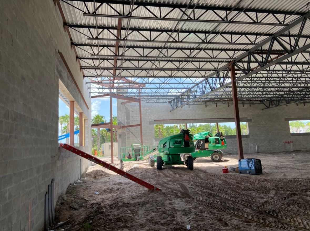 Interior construction: cinder block walls, exposed metal beams, dirt floor, and green machinery.